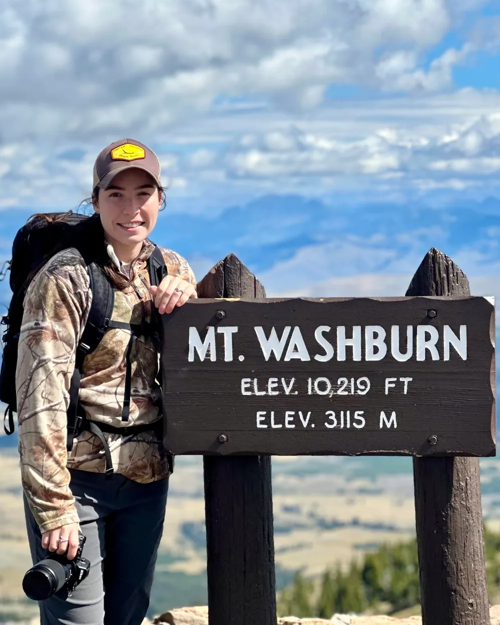 Meredith Lewis at the Mt. Washburn summit sign, camera in hand.