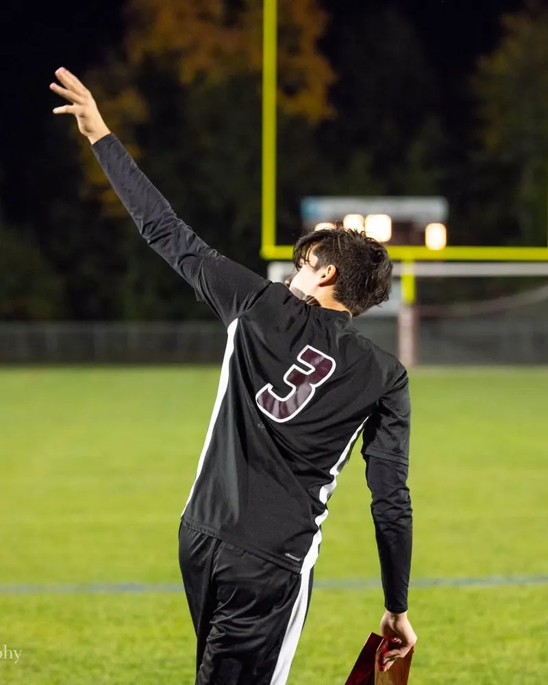 A soccer player in a number 3 jersey raising an arm on the field under the lights at dusk.