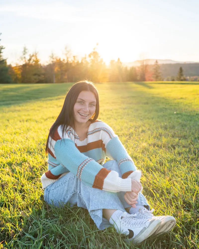 A high school senior standing outdoors among tall grasses during a fall senior portrait session.